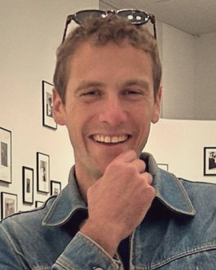 Portrait en couleur d'un homme souriant, la main sous le menton.